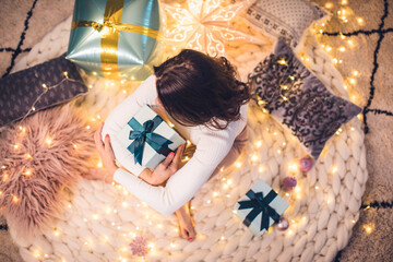 Wall Mural - beautiful young woman with christmas present on knitted carpet with fairy lights for christmas