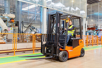 Storehouse employee in uniform working on forklift in modern automatic warehouse. Boxes are on the shelves of the warehouse. Warehousing, machinery concept. Logistics in stock.