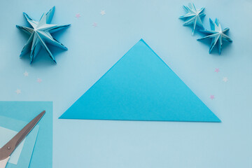 Simple origami 3D Christmas tree made from blue paper. Step by step instruction, step 2. Take the largest square and fold the sheet diagonally with the wrong side inward then unfold it