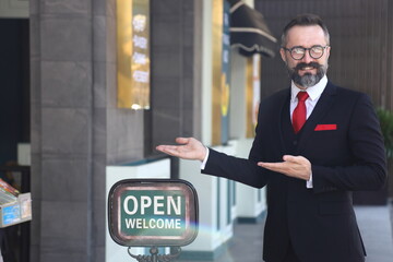 Caucasian waiter standing outside the luxury restaurant with open sign to welcome and greeting the customer	