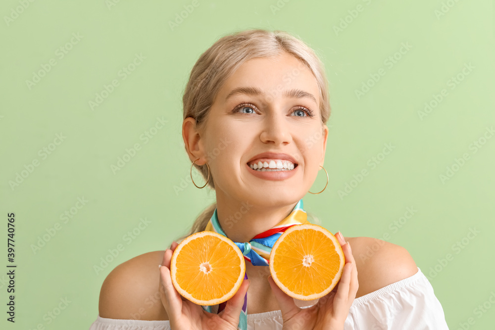 Beautiful young woman with cut orange on color background