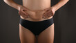 © Tatsiana - Woman in black panties squeezing fat at waist, close-up. Isolated on dark gray background