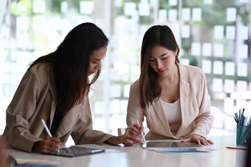 Two business woman are talk about finance and looking graph of economic markets and banks in digital tablet.