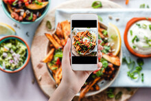 Hand Taking A Photo Of Healthy Food With Smartphone. Woman Using Phone Mobile Apps Make Digital Picture On Screen Of Diet Nutrition Vegan Fruit Granola Seed On Table, Top View