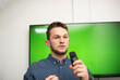 © FarukPhotography - a young caucasian businessman in a shirt wearing glasses presents his presentation, holds a microphone in his hand and talks.