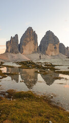 Wall Mural - A man enjoying the sunset over the Tre Cime di Lavaredo (Drei Zinnen) mountains in Italian Dolomites. The peaks reflect in a paddle. The mountains are surrounded with orange and pink clouds. Freedom