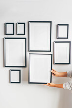 Multiple Many Black Picture Frames On White Wall. Woman Hanging A Frame On A Wall.