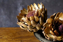 Two Dried Cardoon Heads In A Ceramic Bowl On A Wooden Table Top