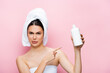 © LIGHTFIELD STUDIOS - disgusted beautiful woman with towel on hair pointing at bottle of lotion isolated on pink