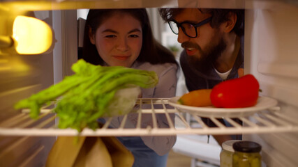 Hungry diverse couple on diet opening fridge and looking at vegetables