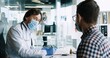 © VAKSMANV - Close up of male physician in medical mask talking on consultation with young patient prescribing treatment sitting at desk in hospital. Rear of young guy at doctor appointment. Coronavirus concept