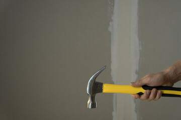 A man holds a yellow hammer against a painted wall. Do home repairs. DIY. Carpenter hands with hammer. Tools for fix the house. Improve your home. To hire a worker for repairs. construction worker