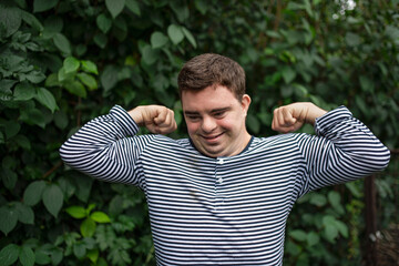 Wall Mural - Portrait of down syndrome adult man standing outdoors at green background, flexing muscles.