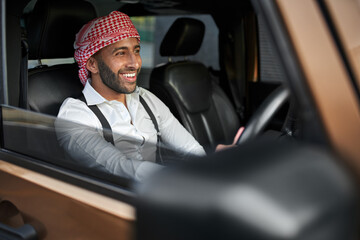 Wall Mural - Smiling arab businessman driving car wearing traditional headscarf keffiyeh