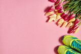 Fototapeta Tulipany - Pair of sport shoes and tulip flowers on pink pastel background, copy space. New sneakers. Overhead shot of running footwear. Top view, flat lay. Spring, sport, minimal concept