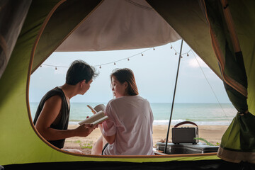 Wall Mural - asian couple camping and reading book on beach with sea background on summer vacation