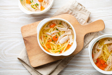 Warm healthy homemade chicken soup in white ceramic bowls on cutting board, white wooden table background. Traditional tasty chicken soup great for health and immune system. Top view