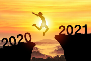 Silhouette sport woman jump through the gap between hill to the new year of 2020 to 2021 on sunset orange sky. happy New year concept. 