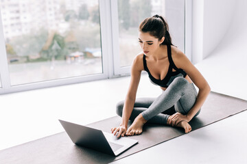 Fit young woman watching online tutorials on laptop, training in living room