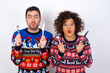 © Roquillo - Model hungry Young couple wearing Christmas sweater standing against white wall holding in hand fork knife want tasty yummy pizza pie