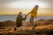 Young Man Making A Marriage Proposal To His Girlfriend On The Mountain Peak At Sunset. 