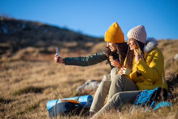 Two young women are resting from hiking and taking a selfie in the mountain.