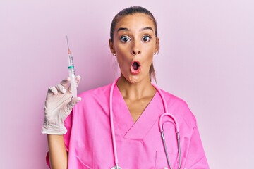 Wall Mural - Young hispanic woman wearing doctor stethoscope holding syringe scared and amazed with open mouth for surprise, disbelief face