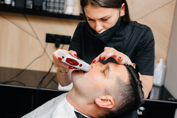 A professional stylist in a modern stylish barbershop shaves and cuts a young man's hair. Beauty salon, hair salon