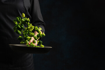 Wall Mural - Chef throws up mix of green cabbage above the pan on dark blue background. Backstage of cooking meal. Frozen motion. Food banner concept. Cookbook illustration