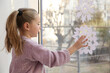 Little girl decorating window with paper snowflake indoors