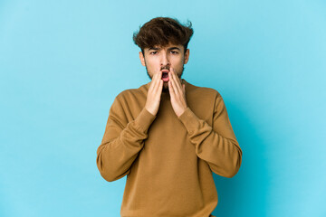 Wall Mural - Young arab man on blue background shocked, covering mouth with hands, anxious to discover something new.