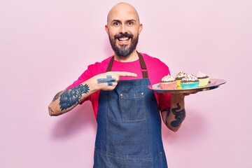 Poster - Young handsome man wearing apron holding cupcake smiling happy pointing with hand and finger