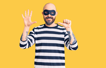 Poster - Young handsome man wearing burglar mask showing and pointing up with fingers number six while smiling confident and happy.