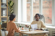 Portrait of smiling African-American woman talking to young woman across table during job interview in office, copy space