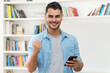 © Daniel Ernst - Cheering hispanic hipster man with beard sending message with phone indoor at home