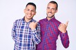 © Krakenimages.com - Young gay couple of two men wearing casual clothes pointing to the back behind with hand and thumbs up, smiling confident