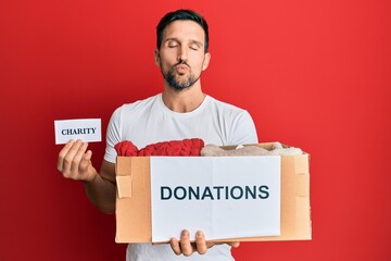 Sticker - Young handsome man volunteer holding donations box with clothes looking at the camera blowing a kiss being lovely and sexy. love expression.