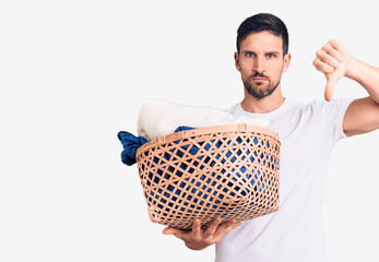 Sticker - Young handsome man holding laundry basket with angry face, negative sign showing dislike with thumbs down, rejection concept