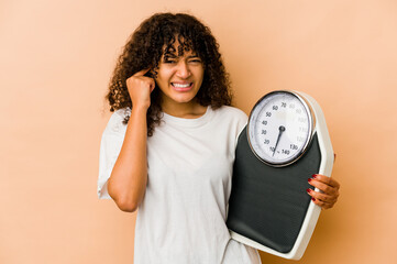 Wall Mural - Young african american afro woman holding a scale covering ears with hands.