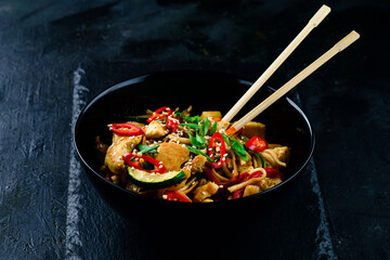 Udon stir fry noodles with chicken and vegetables on black background. hot wok with chicken steaming over plate