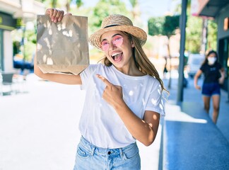 Wall Mural - Young beautiful blonde caucasian woman smiling happy outdoors on a sunny day pointing to delivery paper bag