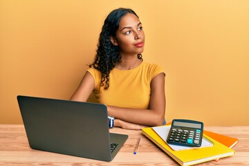 Poster - Young african american girl working at the office with laptop and calculator smiling looking to the side and staring away thinking.
