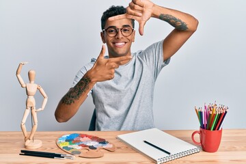 Sticker - Young handsome african american man painter sitting palette and art manikin smiling making frame with hands and fingers with happy face. creativity and photography concept.