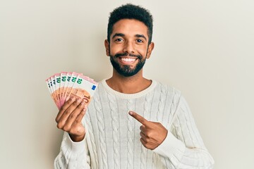 Canvas Print - Handsome hispanic man with beard holding bunch of 10 euro banknotes smiling happy pointing with hand and finger