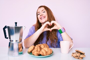 Sticker - Young redhead woman eating breakfast crazy and mad shouting and yelling with aggressive expression and arms raised. frustration concept.