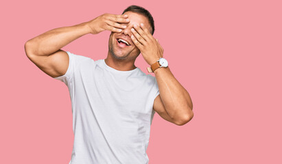 Wall Mural - Handsome muscle man wearing casual white tshirt covering eyes with hands smiling cheerful and funny. blind concept.