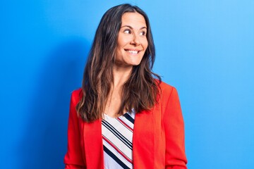 Young beautiful brunette businesswoman wearing jacket standing over blue background looking to side, relax profile pose with natural face and confident smile.