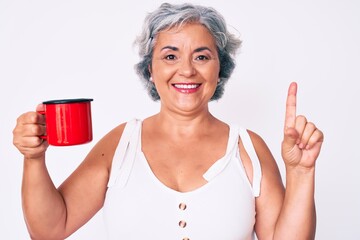 Poster - Senior hispanic woman holding coffee smiling with an idea or question pointing finger with happy face, number one