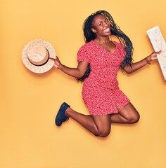 Sticker - Young beautiful african american woman wearing summer clothes smiling happy. Jumping with smile on face holding city map and hat over isolated yellow background.