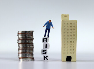 Risk management concept. Miniature man standing on the white cubes with RISK word. Miniature and a pile of coins.
